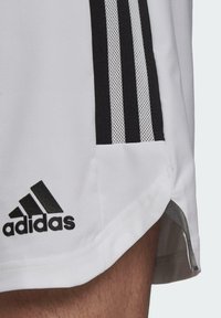 Witte sportshorts gemaakt van ademend materiaal, met zwarte gestreepte accenten en een geborduurd zwart Adidas-logo nabij de zoom.