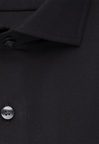 Primo piano di una camicia nera con colletto, realizzata in tessuto strutturato, che presenta un bottone grigio a quattro fori e una silhouette del colletto cucita.