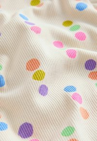 Tela de canalé color crema con lunares de colores dispersos en tonos rosa, morado, azul, verde, naranja y amarillo.