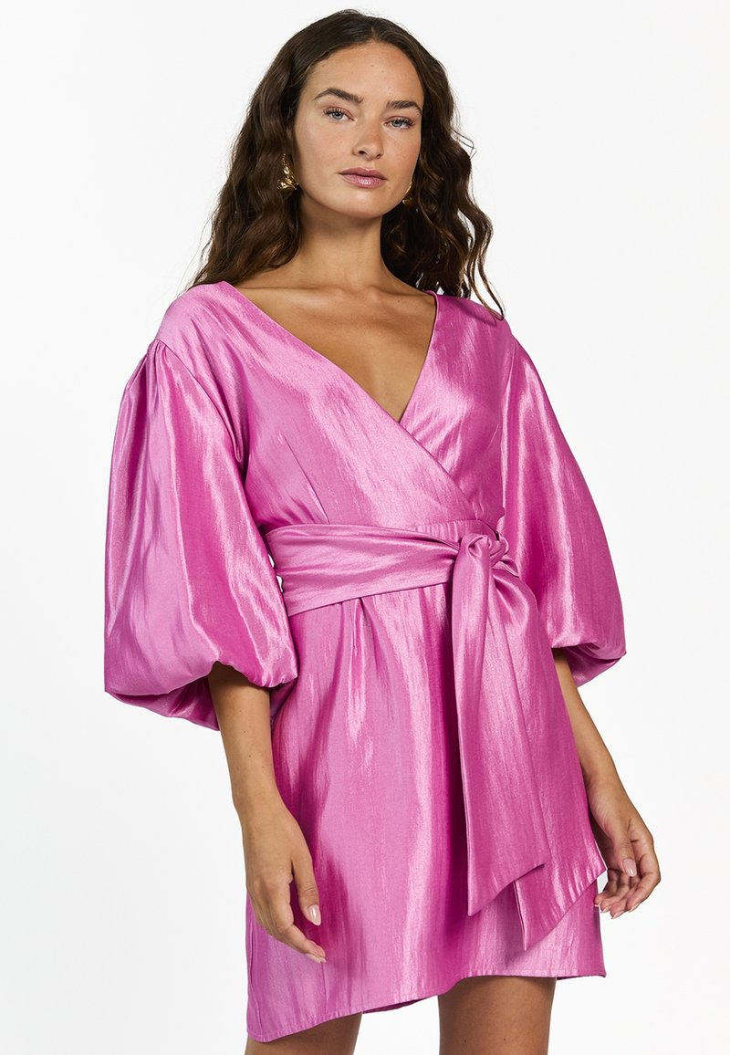 Korte roze jurk van glanzende stof, met ballonmouwen, een diepe V-halslijn en een strikdetail op de taille.