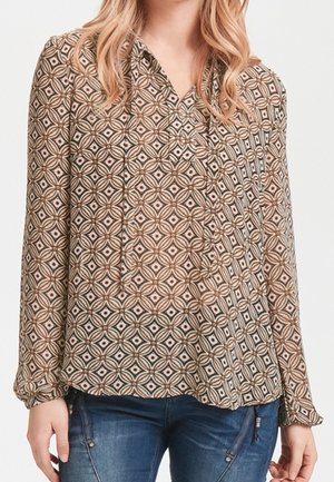 Blusa a maniche lunghe con un motivo geometrico nei colori marrone, crema e ruggine. Caratterizzata da un collo a V e una vestibilità rilassata con una leggera lucentezza.