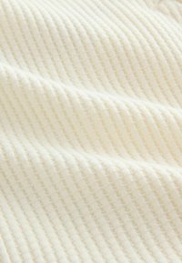 Tejido de punto color crema con una textura acanalada, que presenta líneas espaciadas de manera uniforme y fibras suaves y delicadas.