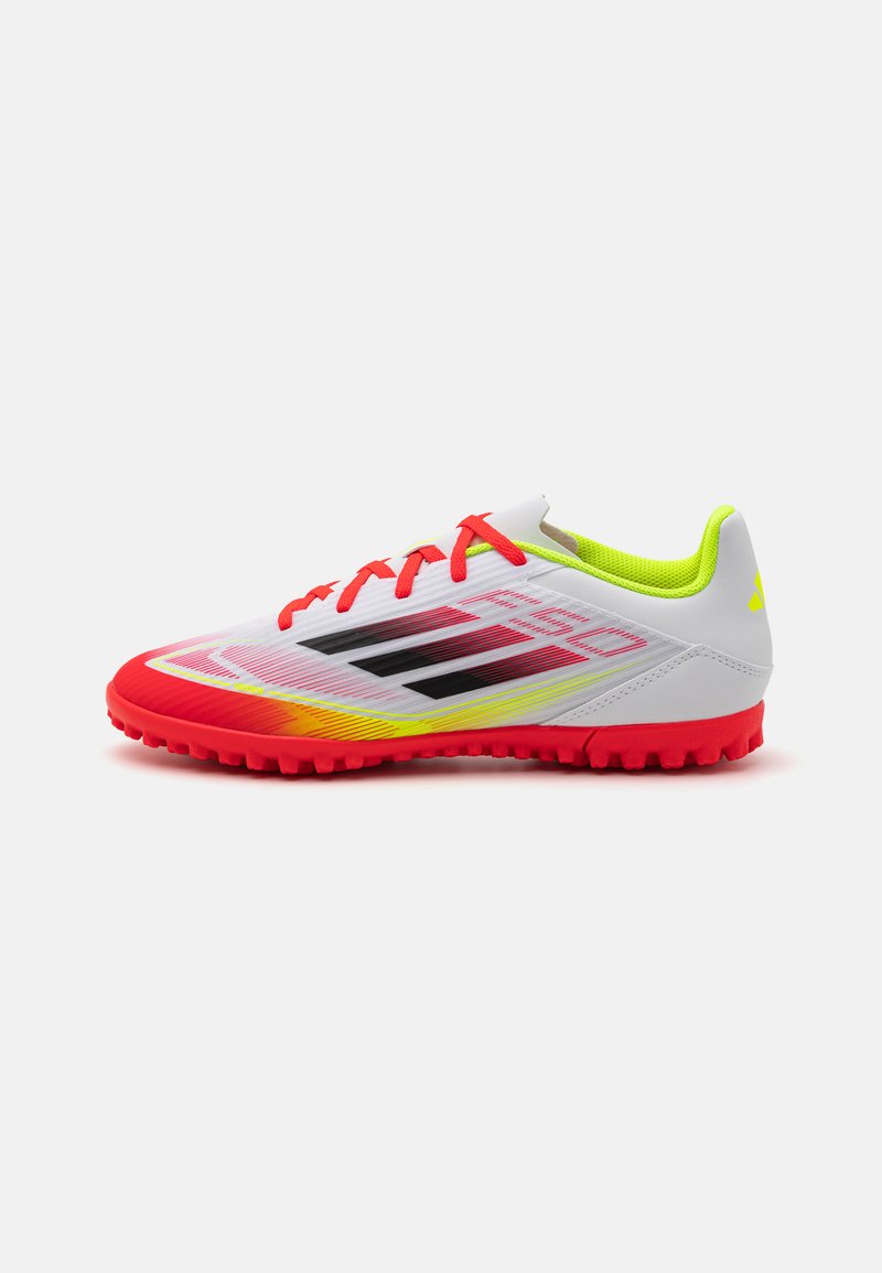 Zapatillas de fútbol blancas con acentos rojos y amarillos. Presentan una parte superior texturizada, franjas negras prominentemente exhibidas y una suela de goma para tracción.