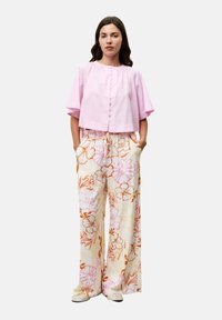 Roze cropped button-up top met korte mouwen, gecombineerd met wijde bloemenbroeken in pastelkleuren en beige instapschoenen.
