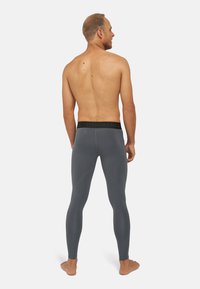 Leggings grises hechos de material elástico, con una cinturilla negra que presenta el nombre de la marca. Textura suave y diseño ajustado.