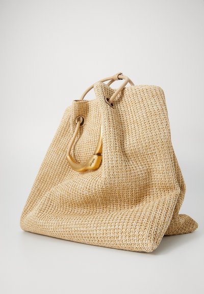 A large, woven beige tote bag with a smooth, curved handle, resting on a light background, showcasing its textured fabric and spacious opening.