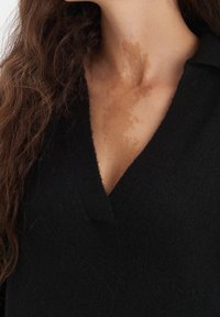 Svart stickad tröja med en djup V-ringning. Har ribbade kanter och en mjuk textur. Modellen har vågigt brunt hår och synliga hudmönster.