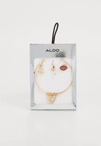 Pulsera de tono dorado con un charm en forma de corazón texturizado con una piedra, acompañada de charms en forma de vaso de cóctel y labios.