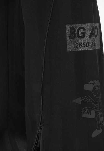 Čierny odev s hladkým materiálom, so zapínaním na zips a reflexnou etiketou s nápisom "BG AD 2650 H." Obsahuje jemný grafický dizajn postavy.