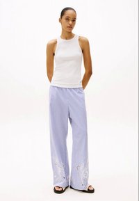 Top sem mangas branco combinado com calças largas listradas em azul claro, com bordados florais nas bainhas. Textura mate, ajuste descontraído.