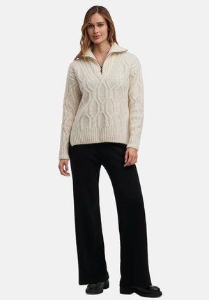 Cream-colored knitted pullover sweater featuring a textured diamond pattern, a half-zip collar, and ribbed hem. Paired with black wide-leg pants.