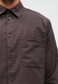 Burgundia ruuduline särk, mis on valmistatud kootud kangast, omab nööpidega kraed, esist pocketit ning tumedaid nuppe, millel on kerge ruuduline muster.