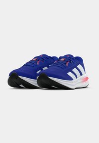 Par blå joggesko med hvite striper og røde detaljer, vinklet fremover på hvit bakgrunn.