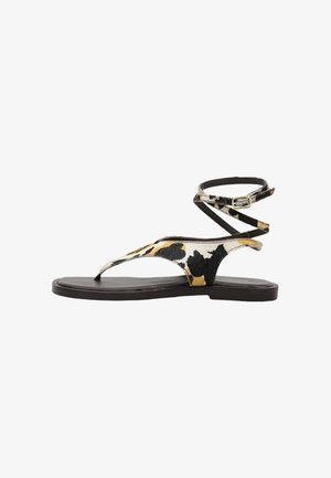 Sandalia plana con tiras de estampado de vaca en negro, blanco y amarillo, y una fina correa para el tobillo con una pequeña hebilla en una suela negra.