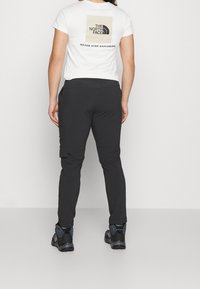 Czarne spodnie cargo o tapered fit, wykonane z lekkiego materiału. W połączeniu z białą koszulką z logo na plecach.