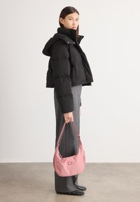 Casaco puffer preto com capuz, design cropped; calças cinzentas com riscas verticais; mala rosa com fecho e logo, calçado preto.