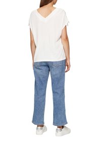 Haut blanc à manches courtes avec un col en V et des accents à nouer aux manches, associé à un jean droit bleu clair et des baskets argentées.
