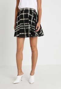 Schwarz-weißer karierten Rock mit einem ausgestellten Design, ausgestattet mit einem gerafften Bund und leichtem Stoff, kombiniert mit weißen Absatzmules.