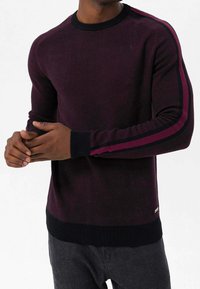 Pull en maille bordeaux foncé avec un col rond, présentant des accents rayés contrastants en bordeaux et noir le long des manches et des poignets côtelés.