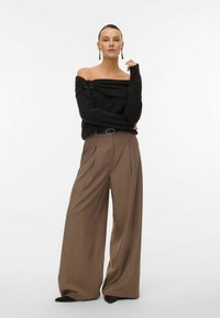 Svart off-shoulder tröja i texturerat tyg, i kombination med högmidjade, vida bruna byxor och svarta spetsiga skor.