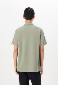 Kortärmad polo shirt i ljusgrön tyg med en slät textur, med en vikbar krage och sydda kanter. Synlig tagg vid nacken.