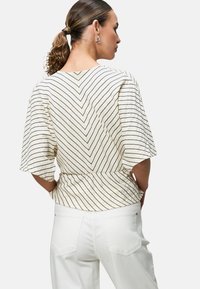White top with black chevron stripes, loose short sleeves, and a waistband. Paired with white pants and a smooth texture.