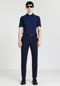 Polo shirt navy a maniche corte, abbinato a pantaloni navy a sigaretta. Una cintura e scarpe nere completano l'outfit. Texture liscia, design minimale.