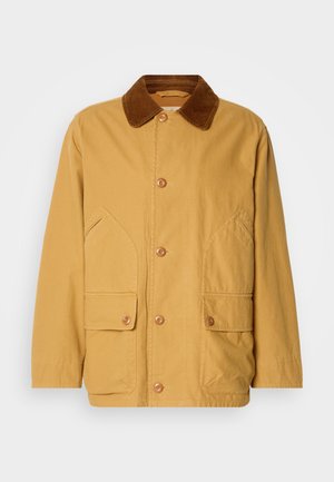 Chaqueta de algodón amarilla con un cuello de pana marrón, grandes bolsillos laterales y cierre de botones en la parte delantera.