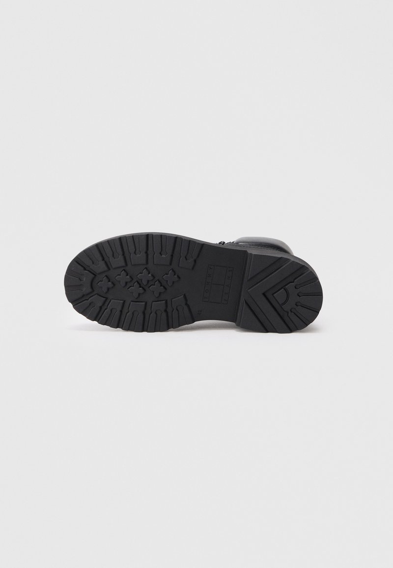 Black boot sole with rugged tread pattern, textured rubber material, and embossed logo detailing; designed for durability and traction.