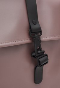 Zaino rosa opaco con chiusura in plastica nera a fibbia. Caratteristiche includono una texture liscia, cuciture sottili e un design minimalista.