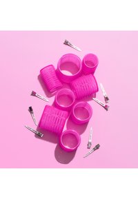 Zestaw różowych plastikowych wałków do włosów w różnych rozmiarach o rowkowanej fakturze, w towarzystwie srebrnych metalowych klipsów do włosów na różowym tle.