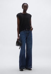 Fekete ujjatlan kötött felső, magas derekú kék farmer, széles szárú nadrág, fekete bőr táska. Egyszerű kialakítás minimális díszítéssel.