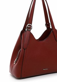 Rote Lederhandtasche mit strukturiertem Finish, trapezförmiger Form, zwei Tragegriffen, silbernem Zubehör und einer seitlichen Reißverschlusstasche.