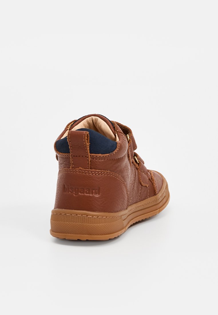 Bottine en cuir marron avec une sangle Velcro, tige texturée, doublure beige et semelle en caoutchouc, avec un logo à l'arrière.