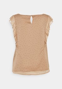 Blouse beige légère à pois noirs, manches volantées, détail dos avec ouverture en forme de goutte, et texture douce et transparente.