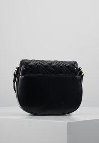 Černá kabelka s kulatým tvarem, vybavená prošívanou koženou klopou a hladkým tělem. Obsahuje jeden nastavitelný popruh a zlaté kovové detaily.