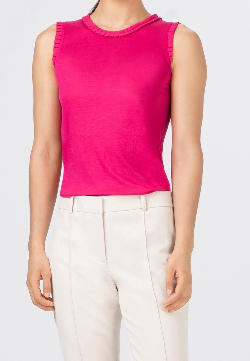 Haut sans manches rose ajusté avec col côtelé et accents d'épaules, associé à un pantalon blanc sur mesure. Tissu lisse et léger.