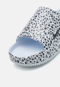 Chinelo de slide com bolas pretas e brancas, design de dedo aberto, textura suave e interior azul claro. Apresenta sola com textura antiderrapante.