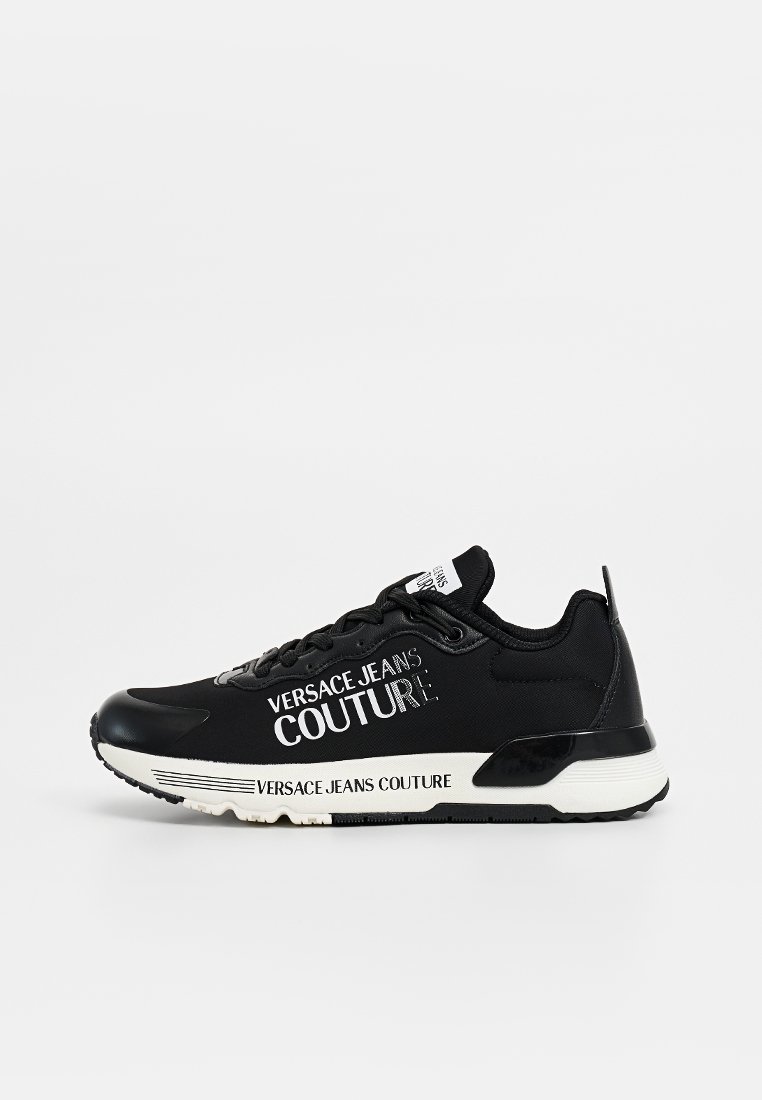 Zapatilla negra con parte superior de tela suave, detalles del logo en blanco y suela de goma. Presenta una lengüeta acolchada y acentos en la suela de color contrastante.