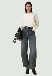 Sweater creme com mangas longas, jeans pretos de cintura alta com bainha desfiada, bolsa preta e botas de tornozelo com bico fino. Design minimalista.