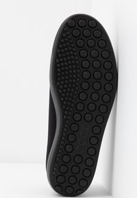 Semelle de chaussure noire avec des motifs de grip circulaires et le nom de la marque "ecco" embossé au centre.
