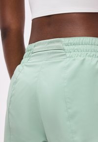 Gros plan d'une personne portant un short vert clair à taille élastique et un top court blanc, montrant le bas du dos et la zone de la taille.