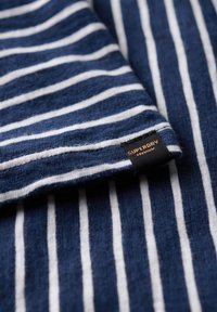 Navyblauw en wit gestreepte stof met een zachte textuur, voorzien van een Superdry premium label op een omgevouwen rand.