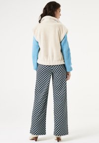 Fleece vest in crèmekleur met blauwe lange mouwen; breedvallige broek met een patroon van zwarte, witte en blauwe driehoeken; hoge hakken.