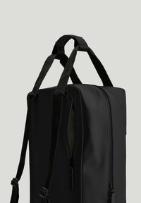 Sort rektangulær rygsæk med to justerbare skulderstropper og en lynlåslomme på siden mod en grå baggrund.