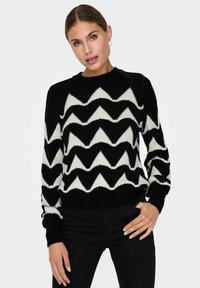 Maglione a zigzag bianco e nero realizzato in morbido materiale maglione, con scollatura rotonda e polsini e orlo a coste.