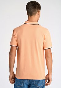 Polo shirt pesca con colletto e polsini neri. Realizzato in tessuto morbido, presenta un taglio pulito e classico con spacchetti laterali.