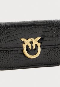 Zwarte leren handtas met een krokodillenstructuur, een gouden ronde hardware detail met twee vogels en een slanke, rechthoekige vorm.