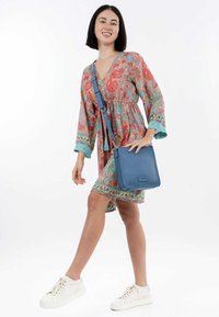 Borsa a tracolla blu in pelle con finitura testurizzata, tracolla regolabile e hardware minimale, abbinata a un vestito floreale colorato e sneakers bianche.