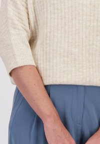 Lichtbeige geribde trui met korte mouwen, gecombineerd met blauwe high-waisted broek. Zachte textuur met subtiele gestreepte details.